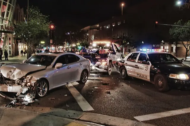 Auto destrozado tras un choque nocturno en una intersección, con una patrulla policial al lado